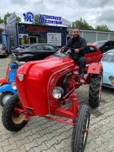 Unser Fachmann von EOS Fahrzeugtechnik posiert vor unserem Standort mit einem klassischen Traktor.
